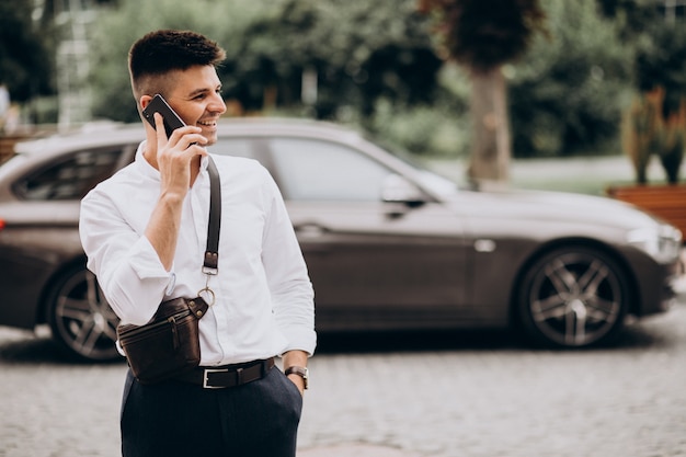 Free photo handsome business man talking on the phone by his car