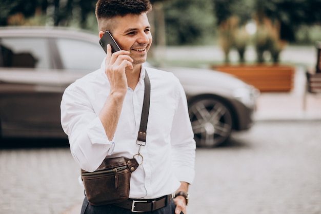 Handsome business man talking on the phone by his car