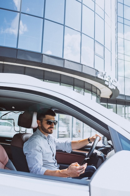 Uomo bello di affari che utilizza telefono nell'automobile