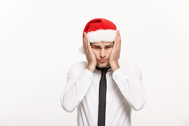 Handsome Business man wearing santa hat posing with stressful facial expression on white.