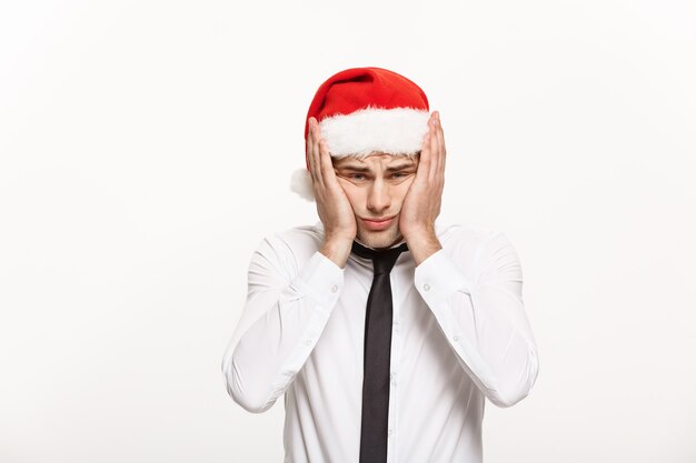 화이트 스트레스 표정으로 포즈 산타 모자를 쓰고 잘 생긴 비즈니스 사람.