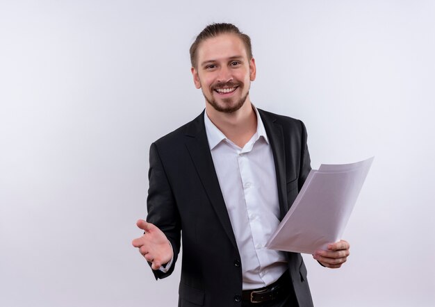 Handsome business man wearing suit holding blank pages looking at camera smiling cheerfully standing over white background