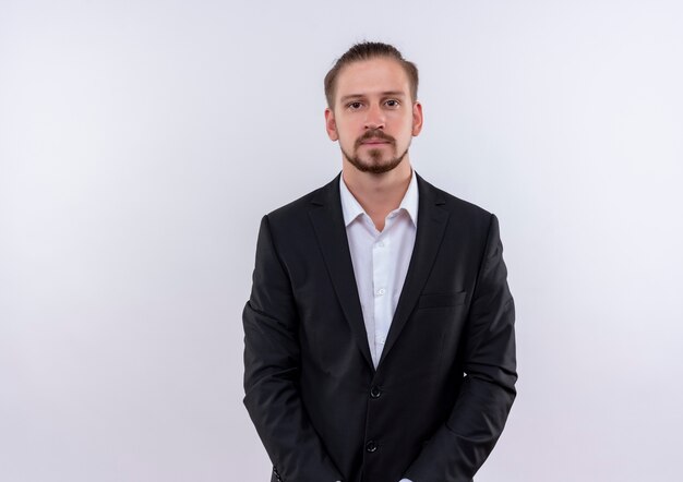 Handsome business man wearing suit loking at camera with serious expression standing over white background