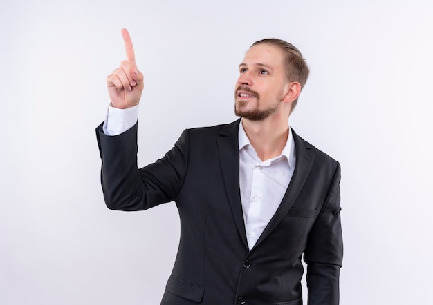 Handsome business man wearing suit looking aside pointing up with index finger standing over white background