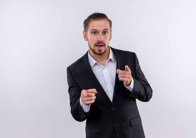 Handsome business man wearing suit looking at camera pointing with index fingers to camera standing over white background