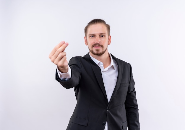 Handsome business man wearing suit looking at camera rubbing fingers making money gesture standing over white background