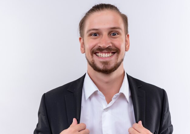 Handsome business man wearing suit looking at camera smiling broadly with happy face standing over white background