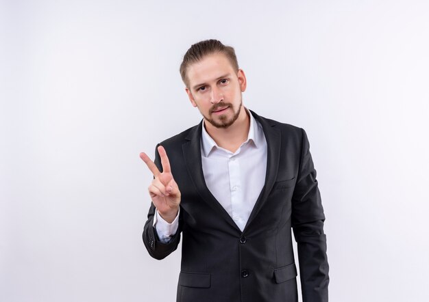 Handsome business man wearing suit looking at camera smiling confident showing victory sign standing over white background