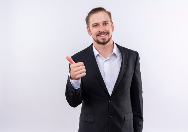 Handsome business man wearing suit looking at camera smiling showing thumbs up standing over white background