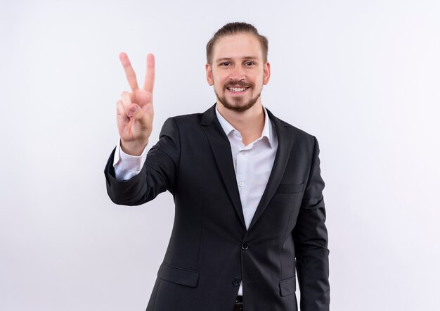 Handsome business man wearing suit looking at camera smiling showing victory sign standing over white background