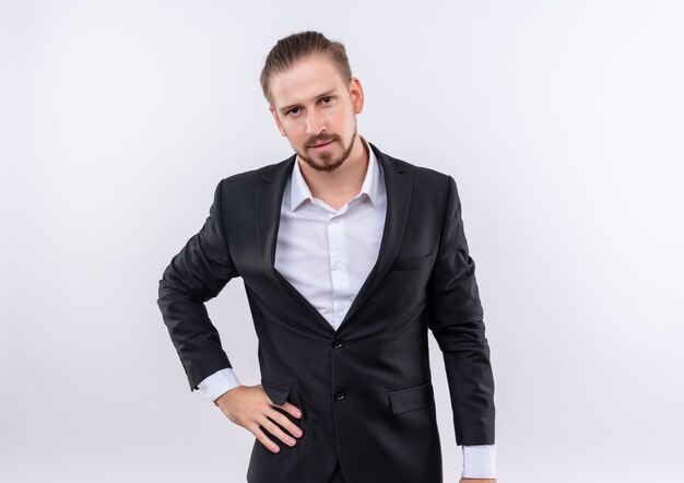 Handsome business man wearing suit looking at camera with serious confident expression standing over white background