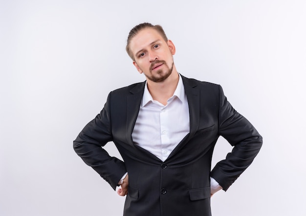 Handsome business man wearing suit looking at camera with skeptic expression standing over white background