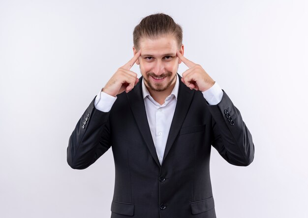 Handsome business man wearing suit looking at camera with smile on face pointing his temples focused on task standing over white background