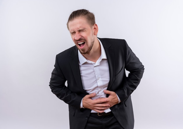 Free photo handsome business man wearing suit looking unwell touching his belly having pain standing over white background