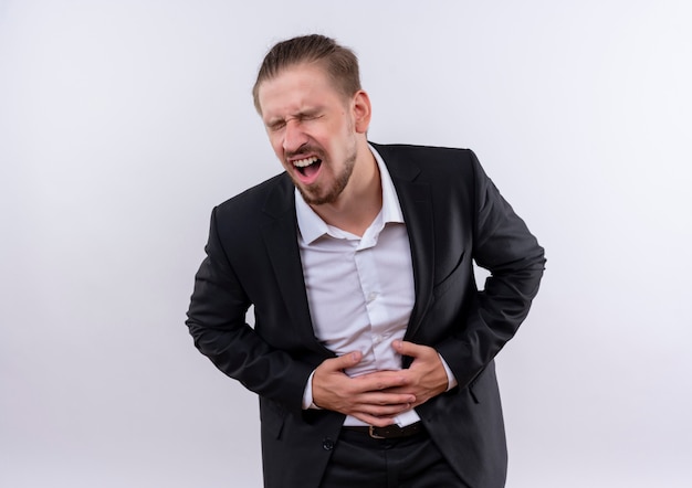 Handsome business man wearing suit looking unwell touching his belly having pain standing over white background