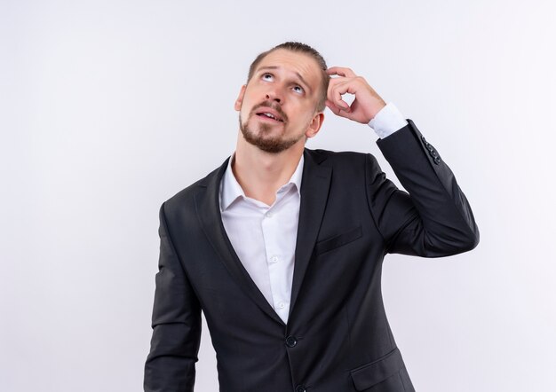 Handsome business man wearing suit looking up with pensive expression standing over white background