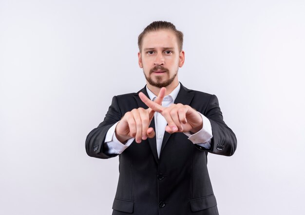 Handsome business man wearing suit making defense gesture crossing index fingers with serious face standing over white background