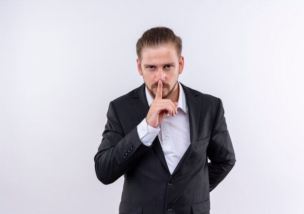 Handsome business man wearing suit making silence gesture with finger on lips standing over white background