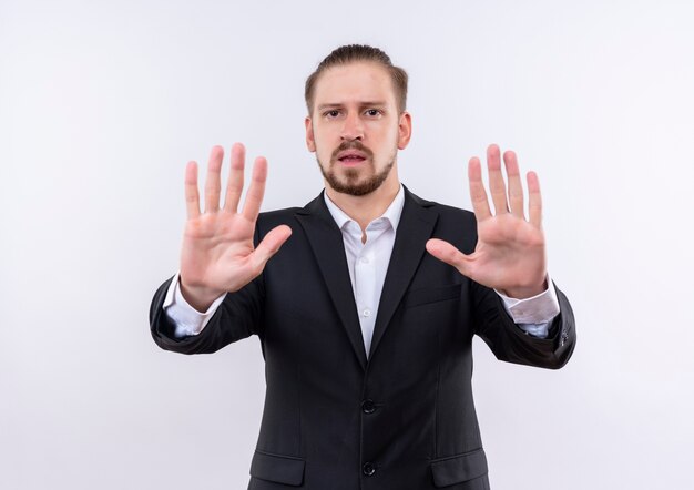 Handsome business man wearing suit making stop sign with open hands looking at camera with serious face standing over white background