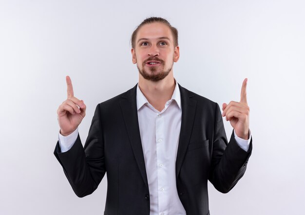 Handsome business man wearing suit pointing up with index fingers happy and positive smiling standing over white background