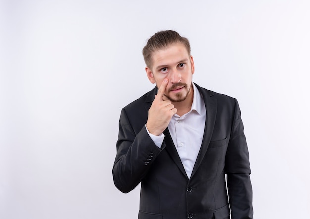 Handsome business man wearing suit pointing with finger to eye watching you gesture standing over white background
