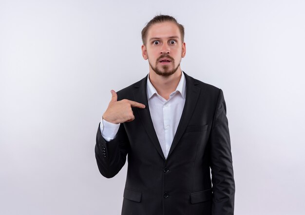Handsome business man wearing suit pointing with finger to himself looking surprised standing over white background