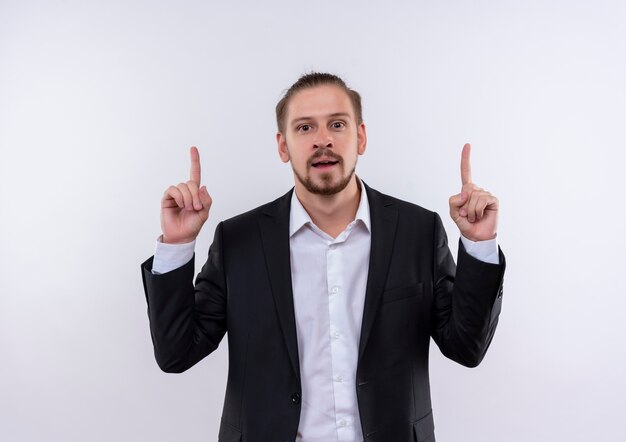 Handsome business man wearing suit pointing with fingers up looking at camera with smile on face standing over white background