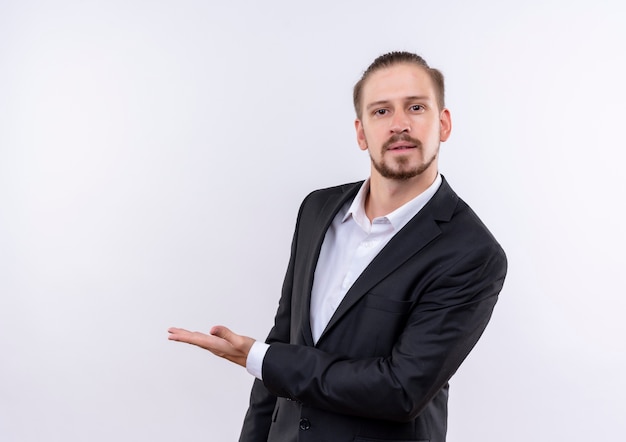 Handsome business man wearing suit presenting with arm of his hand copy space looking at camera with confident expression standing over white background