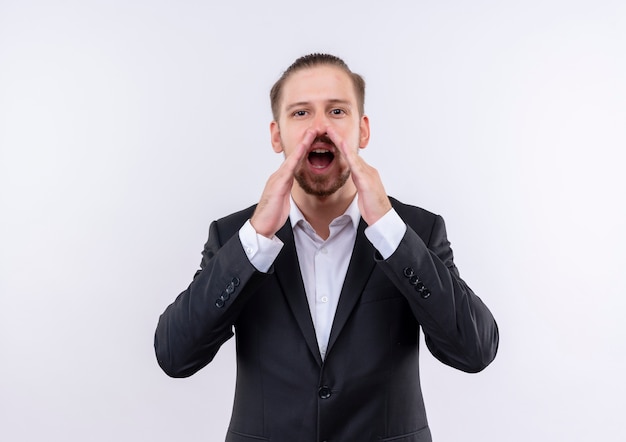 Free photo handsome business man wearing suit shouting or calling someone with hands near mouth standing over white background