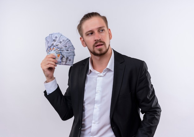 Handsome business man wearing suit showing cash looking aside with confident expression standing over white background