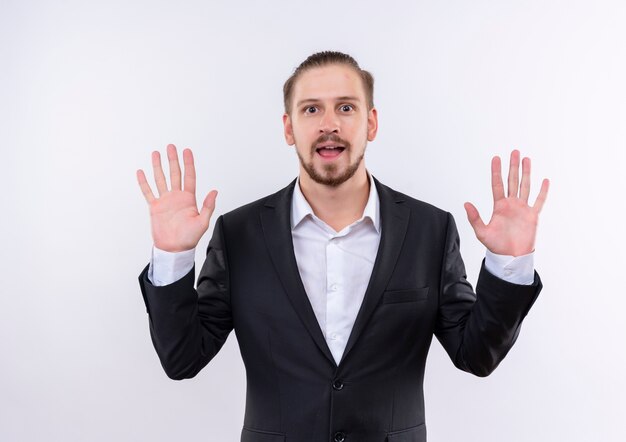 Handsome business man wearing suit showing number ten smiling cheerfully standing over white background