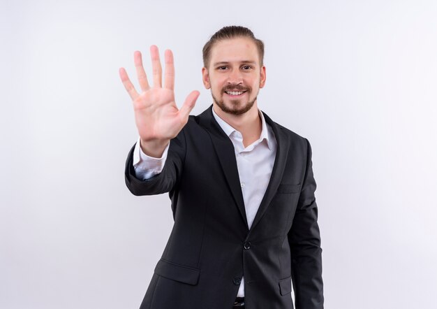 Красивый деловой человек в костюме показывает пальцами номер пять, стоя на белом фоне