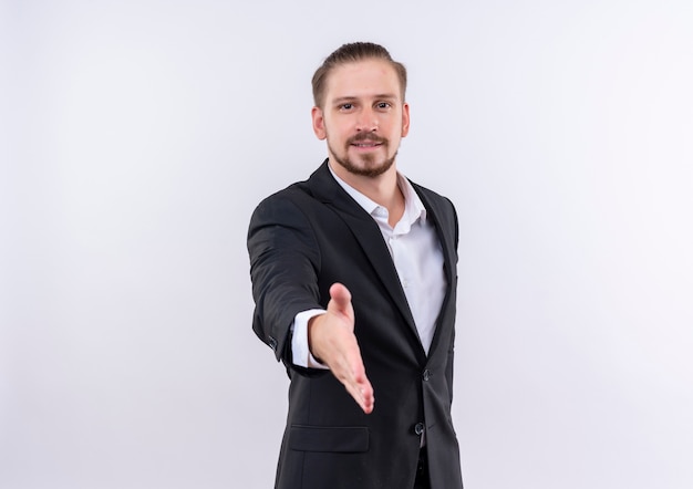 Handsome business man wearing suit smiling friendly greeting offering hand standing over white background