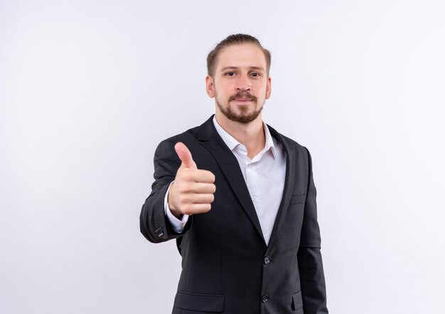 Красивый деловой человек в костюме, улыбаясь со счастливым лицом, показывает палец вверх, стоя на белом фоне
