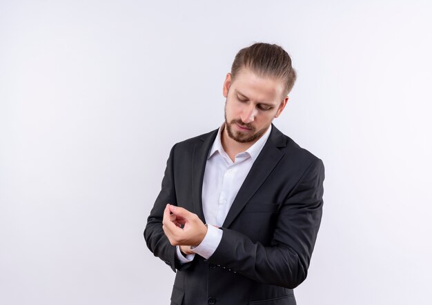 Handsome business man wearing suit touching his cufflinks with serious face standing over white background