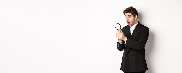 Handsome businessman in black suit holding magnifying glass and smiling found something standing aga