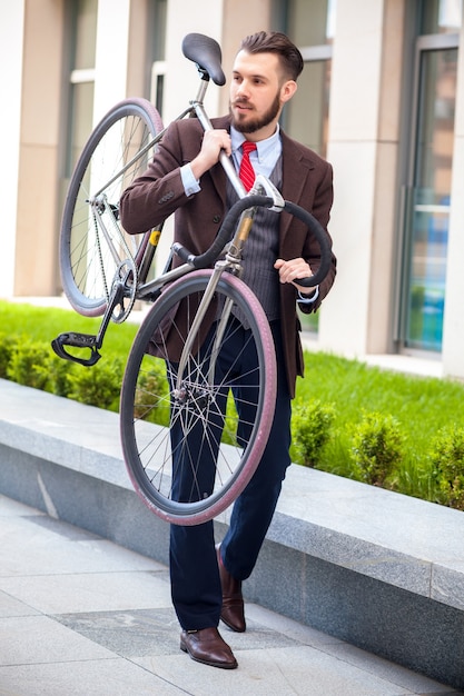 街の通りで彼の自転車を運ぶハンサムな実業家。若い男性の現代的なライフスタイルの概念