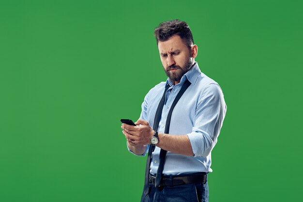 Handsome businessman checking emails on phone. Serious business man standing isolated on green. Beautiful male half-length portrait