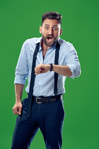 Handsome businessman checking his wrist-watch isolated on green background. Wow