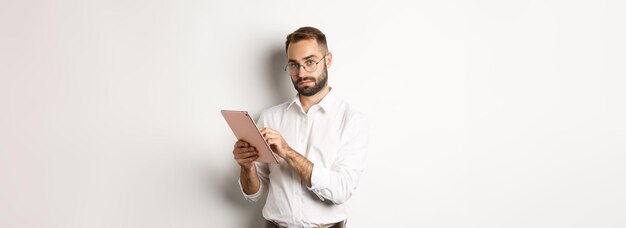 Handsome businessman doing job on digital tablet reading something standing over white background