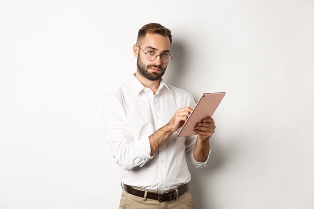 Handsome businessman doing job on digital tablet, reading something, standing  