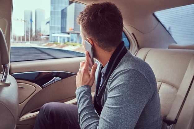 A handsome businessman in elegant clothing working, talking on the phone while sitting in the car.