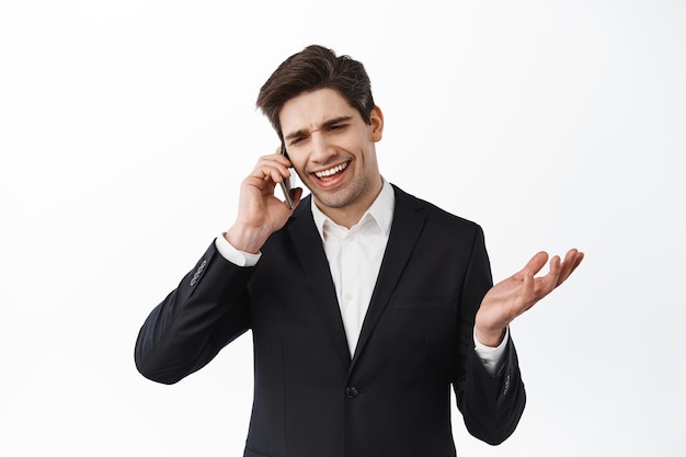 Handsome businessman having business call on mobile phone, smiling and saying yes, give approval, looking satisfied during conversation, white background