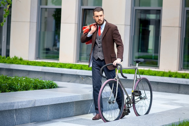 ジャケットと赤いネクタイと街の通りで彼の自転車でハンサムな実業家。若い男性の現代的なライフスタイルの概念