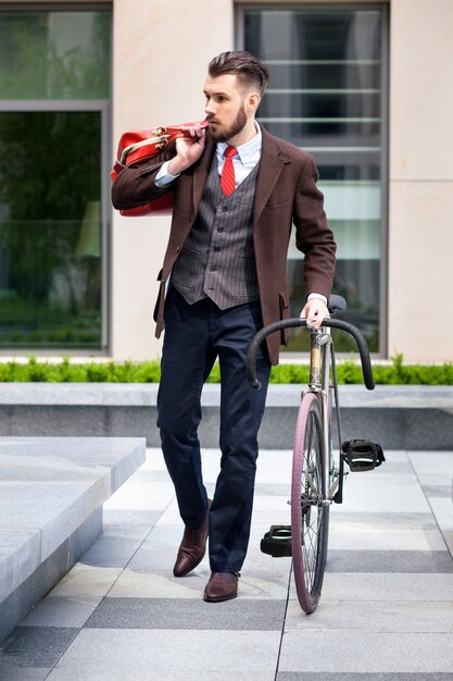 Красивый бизнесмен в куртке и красном галстуке и его велосипеде на улицах города. Концепция современного образа жизни молодых людей