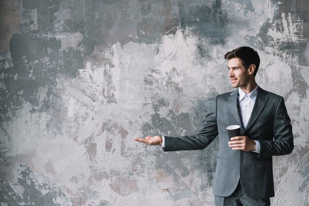 Handsome businessman standing against weathered wall showing something on the palm of her hand