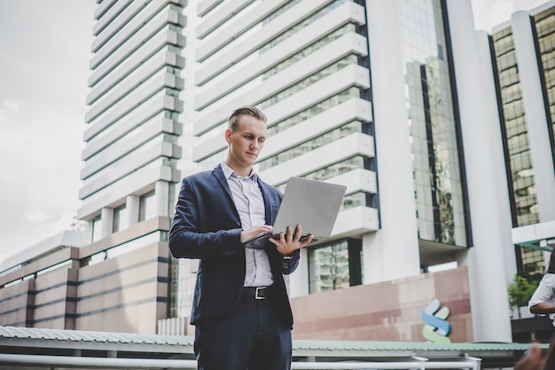 Handsome businessman standing on the way to office with laptop in hand.