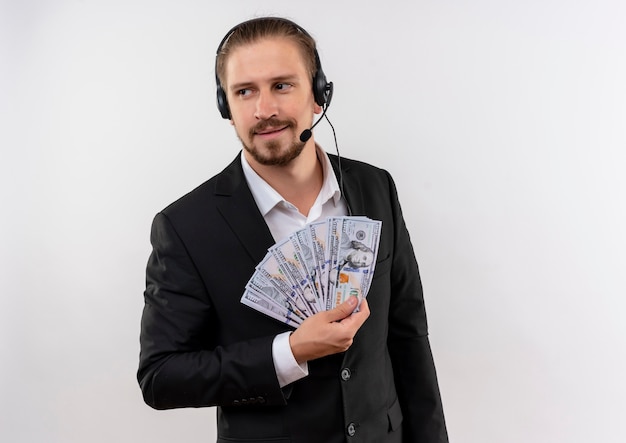 Free photo handsome businessman in suit and headphones with a holding cash looking aside with smile on face standing over white background