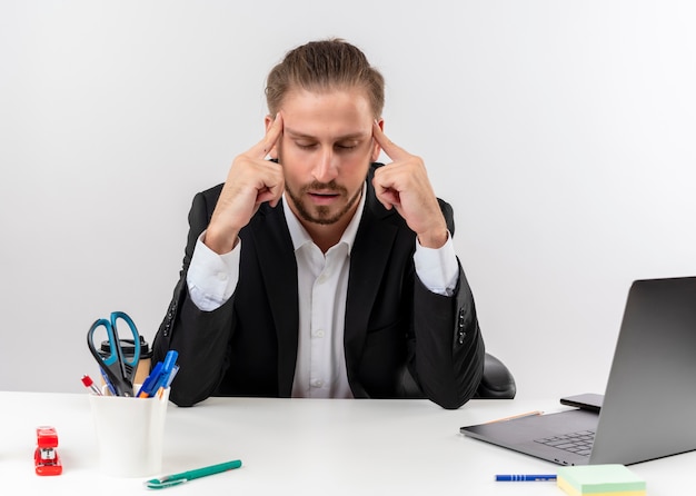 Handsome businessman in suit pointing his temples looking tired and bored sitting at the table in offise over white background