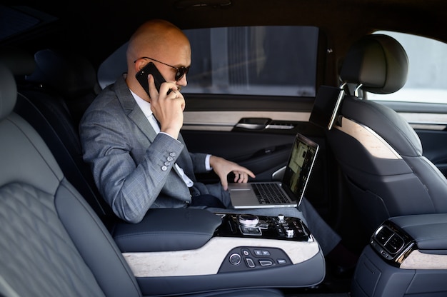 Handsome businessman using his mobile phone in a modern car with a driver in center of the city. concept of business